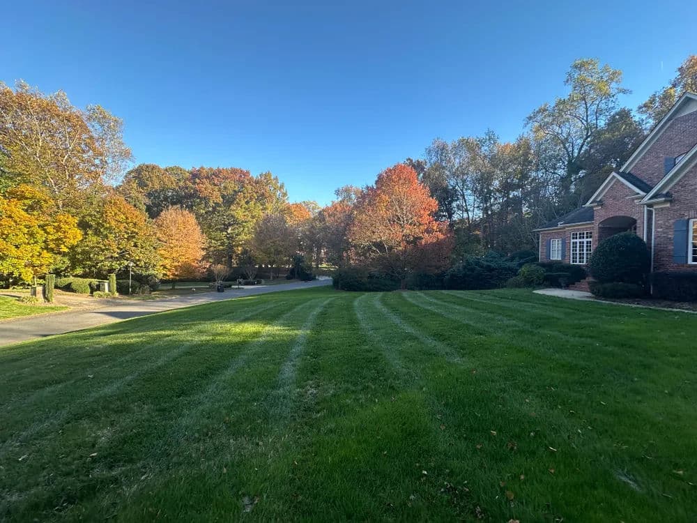 Fall landscape featuring a manicured lawn, colorful autumn trees, and a brick house.