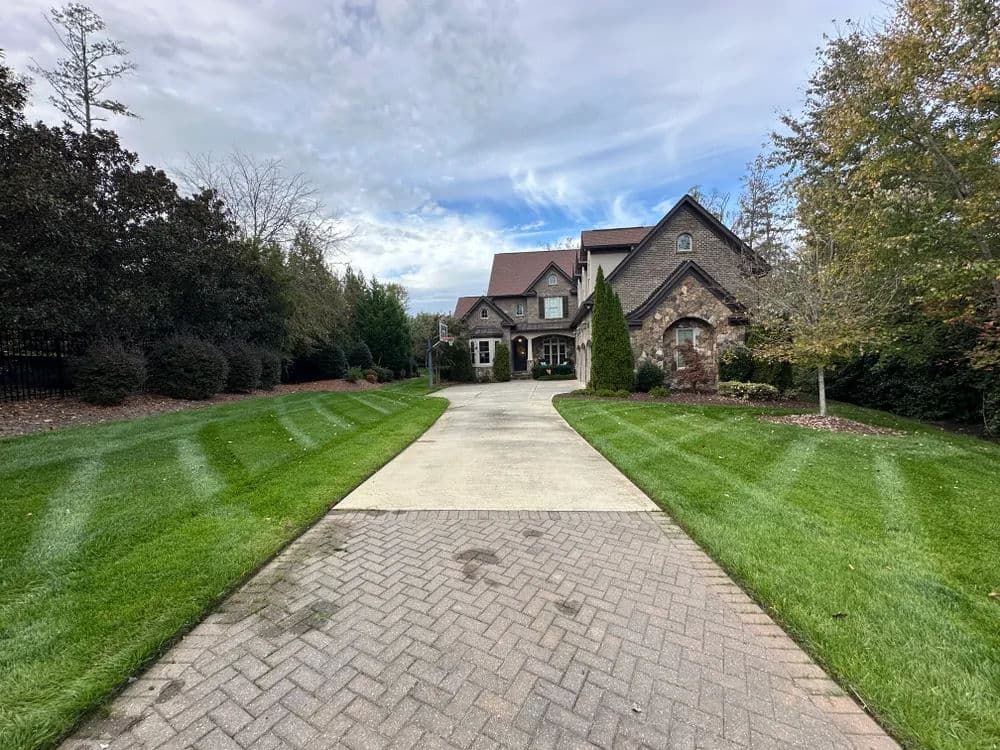 Luxury home with stone facade and manicured lawn, featuring a long paved driveway.