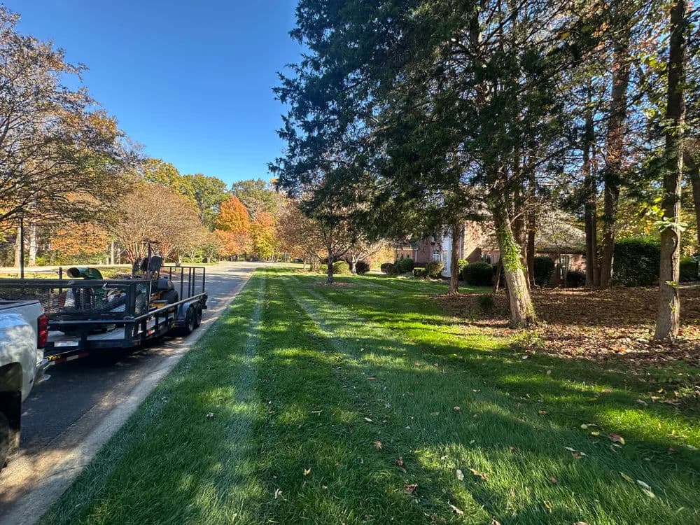 Lush green lawn and autumn trees lining a suburban street with a trailer parked nearby.