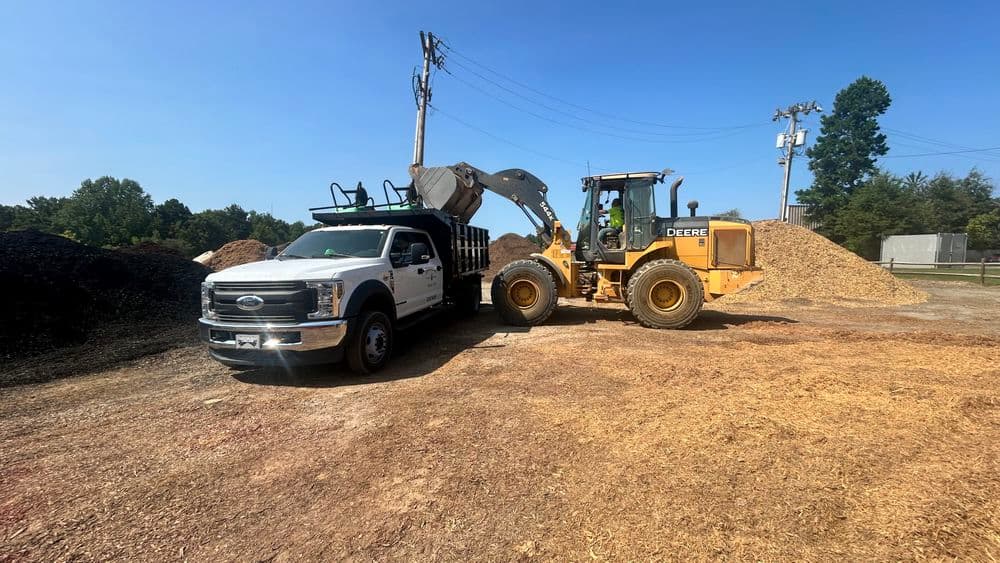 Pickup truck and front loader working together on a construction site with wood chip piles.