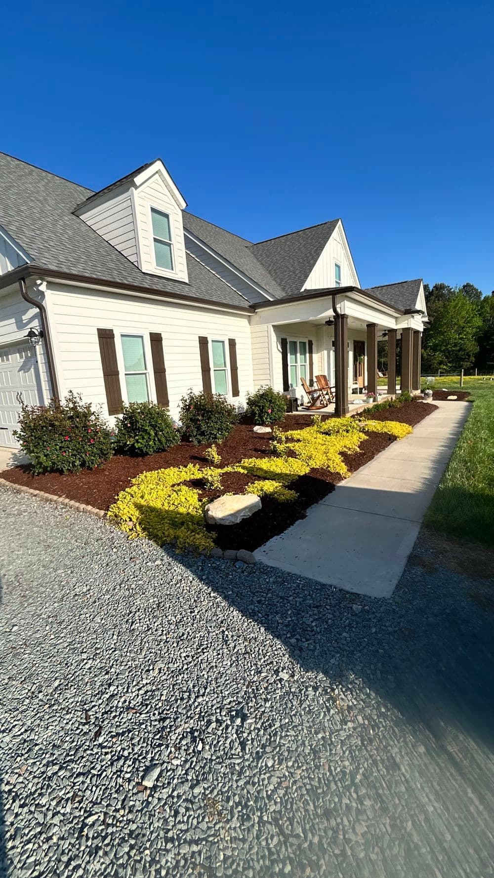 Modern home exterior with landscaped garden, colorful flowers, and gravel driveway.