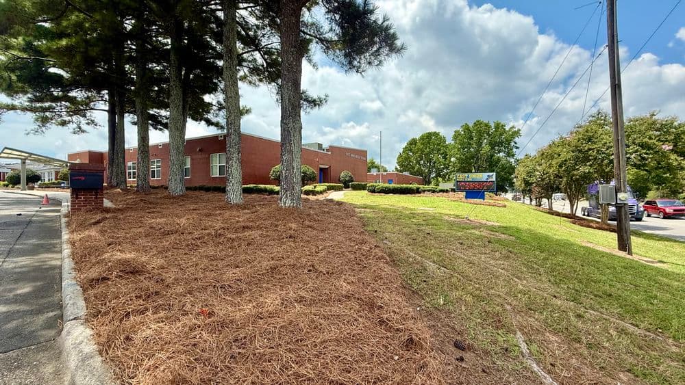Brick building surrounded by trees and landscaped area under a partly cloudy sky.