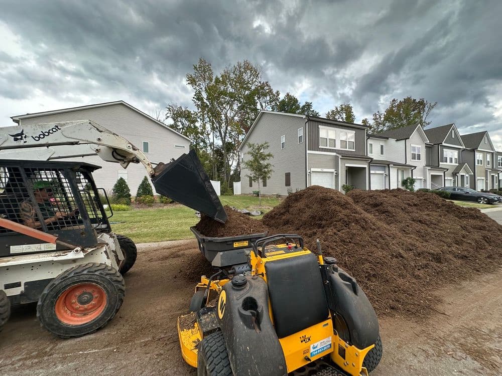 Bobcat loader dumping mulch in a residential area with cloudy skies above.