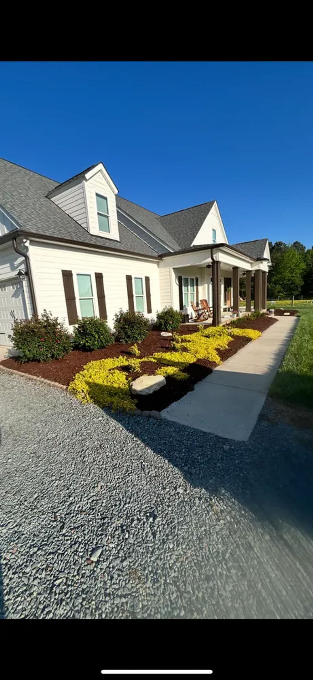 Beautiful suburban home with vibrant flower beds and a welcoming porch under a clear blue sky.