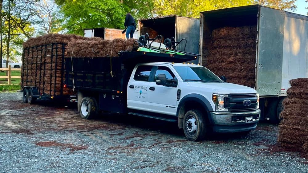 Ford truck unloading bales of hay at a farm, with worker on top of the load.