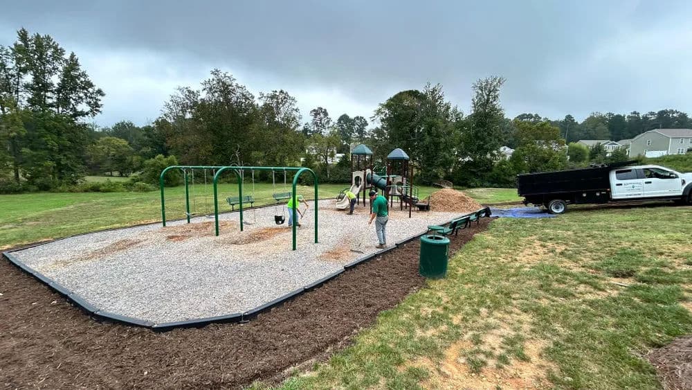 New playground installation with swings, slide, and mulch delivery in a grassy area.